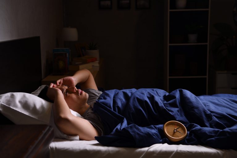 A depressed young man suffering from insomnia lying in bed